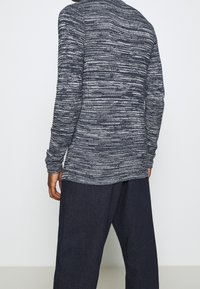 Koszula z długim rękawem wykonana z teksturowanego materiału w granatowo-szarym kolorze. Charakteryzuje się luźnym krojem, okrągłym dekoltem i jest zestawiona z ciemnymi spodniami.