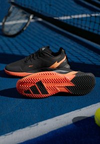 Μαύρα αθλητικά παπούτσια με πορτοκαλί λεπτομέρεια, υφασμάτινο άνω μέρος με υφή και μοτίβο στην ελαστική σόλα. Διαθέτουν αε streamlined σχεδίαση για σπορ.