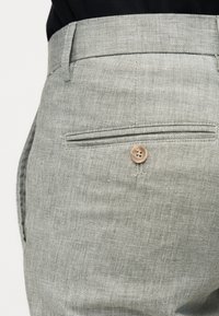 Κοντινό πλάνο ανοιχτόγκρι υφασμάτινου παντελονιού με κουμπωμένη πίσω τσέπη και θηλιές για ζώνη.