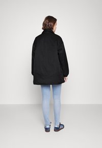 Sort, oversized pufferjakke med høj krave, glat tekstur og lange ærmer, parret med lyseblå slim-fit jeans og sneakers.
