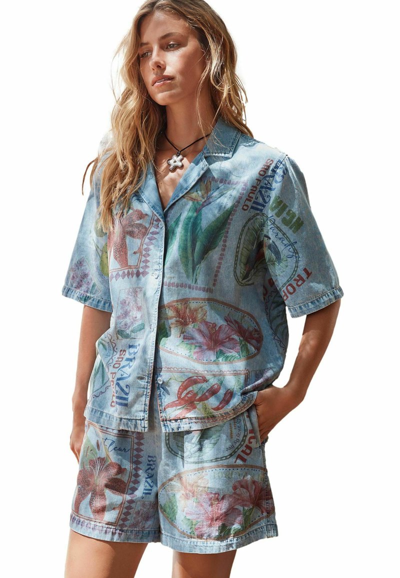 Ensemble chemise en jean et short de couleur bleu clair, orné de motifs floraux et de détails graphiques. Manches courtes et coupe décontractée.