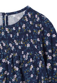 Dunkelbluse mit floralen Mustern und Rüscheldetails; weist kleine weiße und gelbe Blumen zwischen grünen Blättern auf; gerundeter Halsausschnitt mit Schlüsselaugenverschluss auf der Rückseite.