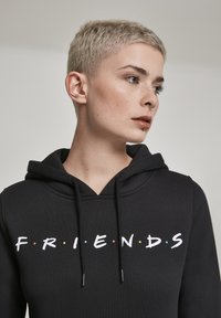 Black hoodie with a wide neckline, featuring the word "FRIENDS" in white letters and colored dots, made from a soft, textured fabric.