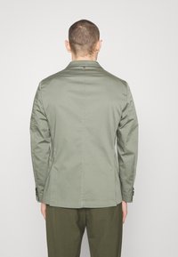 Olivgrüne Jacke mit taillierter Passform, langen Ärmeln, Reverskragen und Knopfdetails an den Manschetten. Glatte Stofftextur.