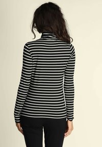 Maglione a maniche lunghe con colletto a imbuto a righe bianche e nere, caratterizzato da un design aderente e una texture morbida, indossato con pantaloni neri.