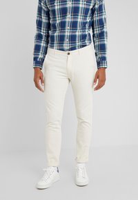 Chinos blancs coupe slim, fermeture à boutons, avec poches avant. Associés à une chemise à carreaux bleue et verte et des baskets blanches.