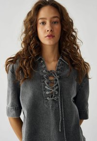 Top in denim grigio con scollatura a laccio e occhielli in argento, maniche corte e vestibilità rilassata, che presenta una finitura testurizzata.