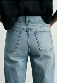 Jean en denim bleu clair à taille haute, avec des poches arrière et une texture légèrement délavée, associé à un haut noir couvrant une partie de la taille.