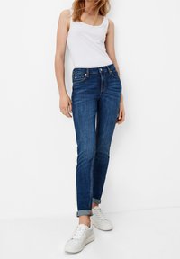 Tmavě modré džíny slim fit, s pěti kapsami, poutky na opasek a ohrnutými nohavicemi, doplněné bílým t ílkem a bílými teniskami.