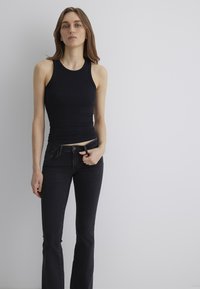 Black ribbed tank top paired with dark denim flared jeans. Fitted design with a smooth texture, featuring a slight stretch and minimal hardware.