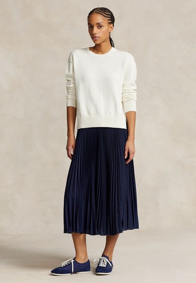 Kremiškas megztinis su ribbinguota apačia, derinamas su tamsiai mėlyna plisėta sijonu ir mėlynomis sportinėmis su baltais raišteliais. Tekstūruotas mezginys ir lengvai krintanti medžiaga.