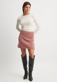 Pletena roza krila s reberčastim pasom, v kombinaciji z oprijetim dolgim belim topom in črnimi usnjenimi škornji do kolen.