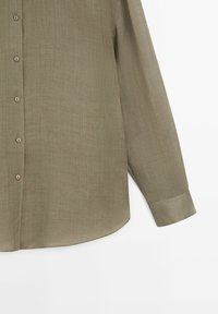 Olijfgroen langemouwen shirt met een zachte textuur, knoopsluiting en een gebogen zoom. Heeft een enkele knoop op elke manchette.