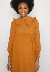 Vestido laranja texturizado com gola em babados e mangas bufantes. Cintura franzida, tecido macio e um corte relaxado.