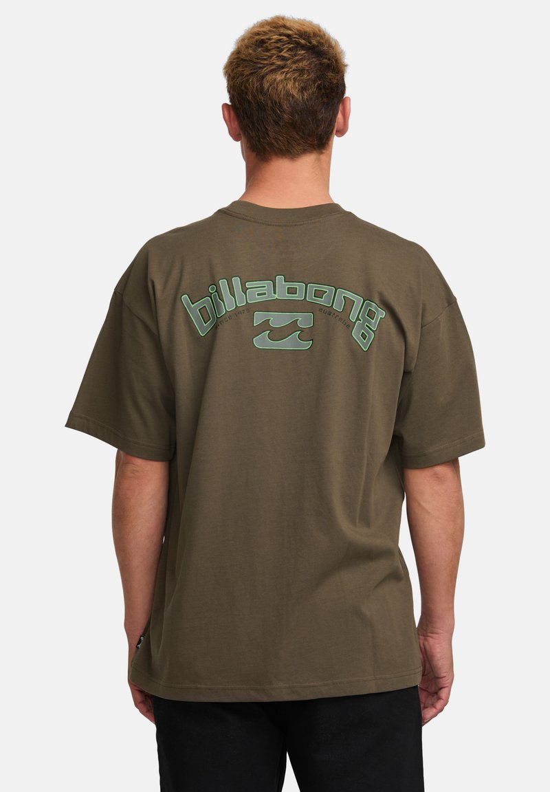 Olive green oversized t-shirt featuring white and teal "Billabong" logo and wave design on back. Made of soft, breathable fabric.