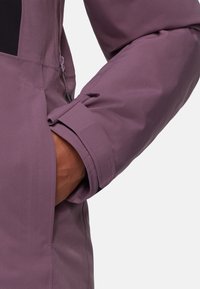 Lila Textiljacke mit einem Nahaufnahme des Bündchens, das einen Reißverschluss und eine glatte, matte Oberfläche zeigt.