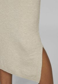 Vestido beige hasta la rodilla en suave tejido de punto texturizado, con una abertura lateral para mayor comodidad de movimiento y un dobladillo redondeado.