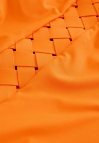 Oranje stof met geweven accenten, een gladde textuur en een levendige kleur. Het ontwerp bevat vlakke secties en ingewikkelde weefdetails.