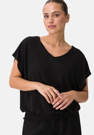 Schwarzes V-Ausschnitt-Oberteil mit kurzen Ärmeln, leichtem Stoff, lockerer Passform und gerafftem Saum. Glänzende Textur kombiniert mit gemusterten schwarzen Hosen.