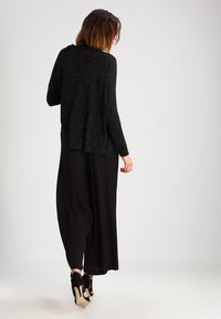 Cárdigan negro de punto con corte holgado, mangas largas y detalles texturizados. Combinado con pantalones de pierna ancha negros y zapatos de tacón.