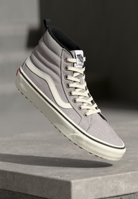 Gray high-top sneaker featuring suede material, white side stripe, round laces, prominent stitching, and textured sole with a pull tab at the back.