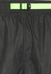 Svarta shorts i lätt material med rutmönster, utrustade med ett justerbart neon grönt bälte och elasticitet i midjan.