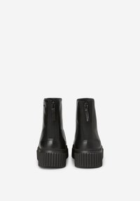 Bottines en cuir noir avec une semelle nervurée et une fermeture éclair sur le côté. Texture lisse et design à bout rond.