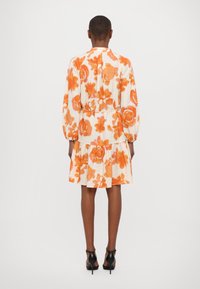 Blumenkleid in Weiß mit orangen Blumen, langen Ärmeln und einem gestuften Rüschensaum. Hergestellt aus leichtem Stoff mit einer lockeren Passform.