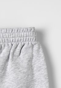 Grå bomullsduk med elastiskt midjeband och samlad sömnad, troligtvis en del av avslappnade eller sportiga byxor eller shorts.