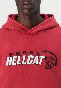 Roter Kapuzenpullover aus Baumwolle; mit "DODGE HELL CAT" in fettem Schwarz- und Weißdruck, dazu ein schwarzes Grafikdesign des Hellcat-Logos.
