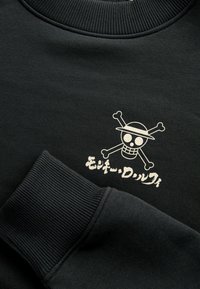 Czarny sweatshirt z białym wzorem czaszki i piszczele, z czapką i tekstem w zabawnym kroju pisma. Żebrowane mankiety i dekolt.