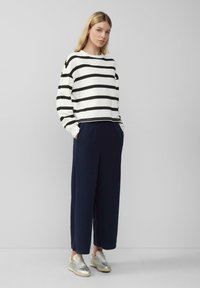 Gestreept sweater in wit en zwart, gecombineerd met marineblauwe wijde broek. Schoenen hebben metallic accenten. Casual en relaxte pasvorm.