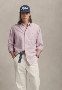 Svetlo roza prugasta srajca z gumbi, bele hlače, mornarsko modra kapa z logotipom "Ralph", multikolor prugast pas, srečna ura na zapestju.