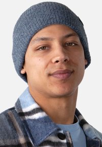 Bonnet en tricot gris sur une personne, portant une chemise à carreaux bleu clair avec des rayures bleu foncé et bleu clair. Texture de tissu lisse.
