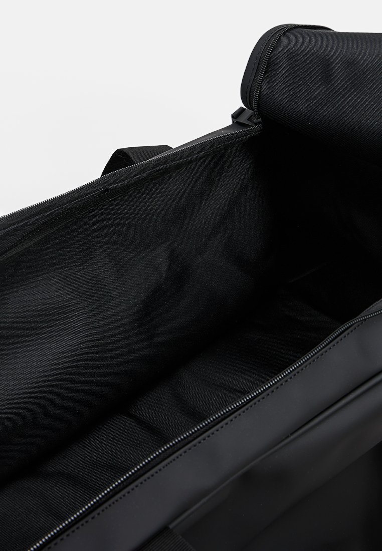 Sac de sport noir avec un grand compartiment ouvert, tissu lisse, fermeture éclair robuste et doubles poignées pour un transport facile. L'intérieur est doublé de matière noire.