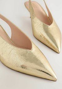 Décolleté slingback in pelle cracklè dorata, con punta affilata, tacco basso e design aperto sul retro. Fodera interna liscia.
