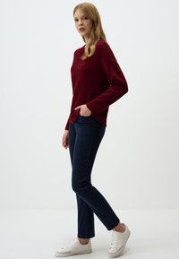 Pull en maille côtelée bordeaux au fit décontracté, associé à un pantalon slims bleu marine et des baskets blanches, mettant en valeur des lignes et des textures épurées.