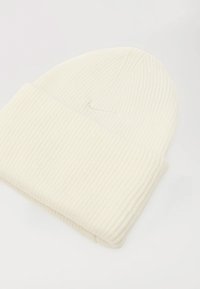 Ribbed cream-colored knit beanie with a folded cuff. Made from soft fabric, features a subtle logo detail on the front.