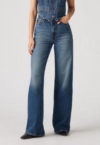 Lysvaskede denimjeans med høy midje, vide ben og kontrastfarget søm. Har frontlommer og knappelukking.