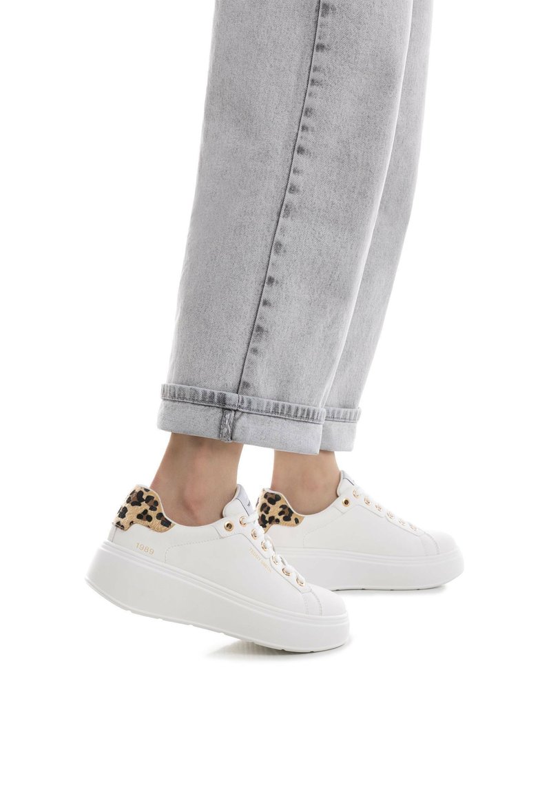 Zapatillas de plataforma blancas con acentos de estampado de leopardo en el talón, ojales en tono dorado y textura suave. Combinadas con unos vaqueros grises remangados.