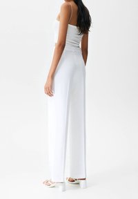 Białe spodnie o szerokich nogawkach i wysokim stanie, gładki materiał oraz prosta sylwetka. W zestawie z białymi sandałami na obcasie. Minimalistyczny design.