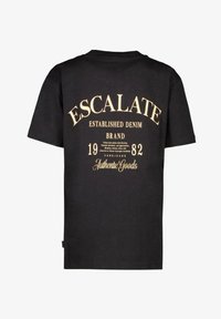 Zwarte katoenen t-shirt met crèmekleurige tekst die "ESCALATE" en "BEKEND DENIM MERK" omvat, met een jaar en aanvullende details.