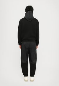 Svart genser med en teksturert grå hette, kombinert med svarte smale bukser med blanke detaljer. Hvite sneakers fullfører antrekket.