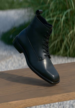 Black leather ankle boot with a smooth finish, round toe, and lace-up design. Features a pull tab at the back and a wooden platform.