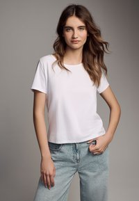 Witte T-shirt met korte mouwen, ronde hals, gemaakt van zacht materiaal, gedragen met lichtblauwe high-waisted spijkerbroek, met een ontspannen pasvorm.