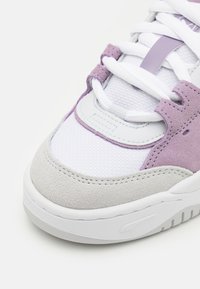 Sneaker viola e bianca con tomaia in suede, sezioni in rete e puntale grigio texturizzato. Lacci bianchi e collo imbottito aumentano il comfort.
