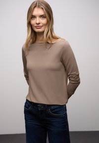 Beiges Langarmshirt mit rundem Ausschnitt und eng anliegenden Ärmeln, kombiniert mit dunkelblauen Jeans im klassischen Five-Pocket-Design.