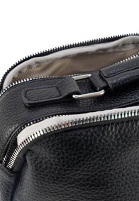 Zwarte gestructureerde leren tas met een zilveren rits, met een klep en metalen hardware; interieur heeft een visgraatpatroon voering.