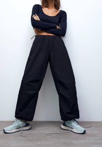Zwarte, loszittende cargos met een elastische tailleband; gecombineerd met lichtblauwe sportschoenen en een strak zwart shirt met lange mouwen.