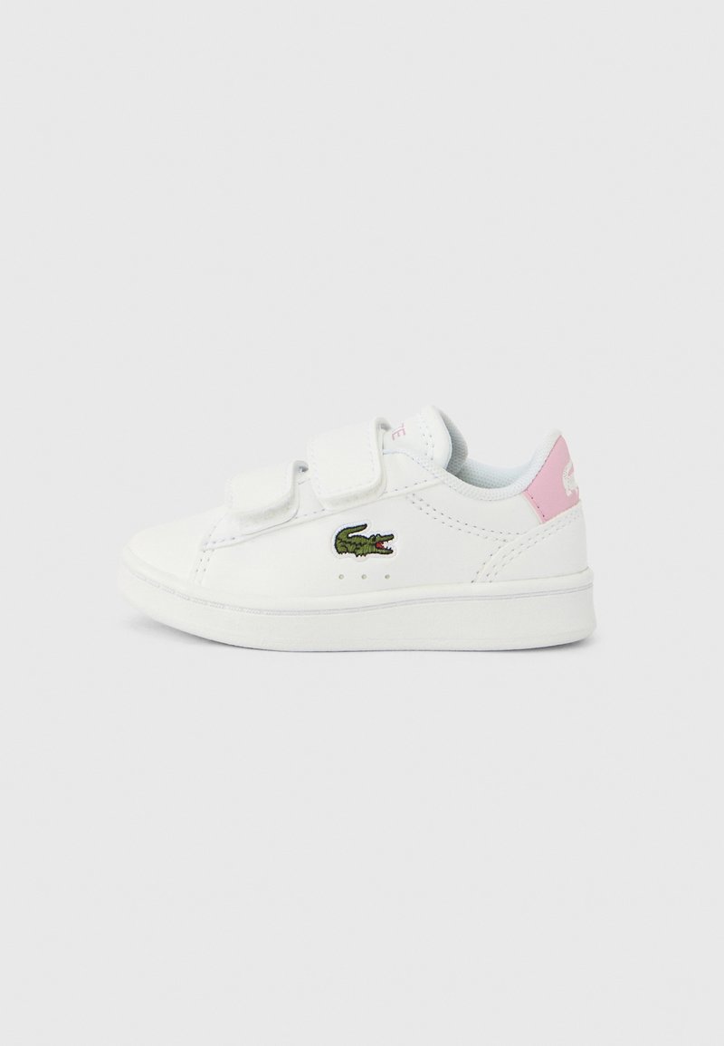 Baskets blanches avec fermetures Velcro, présentant un logo crocodile vert brodé, un accent rose au talon, et un matériau synthétique lisse.